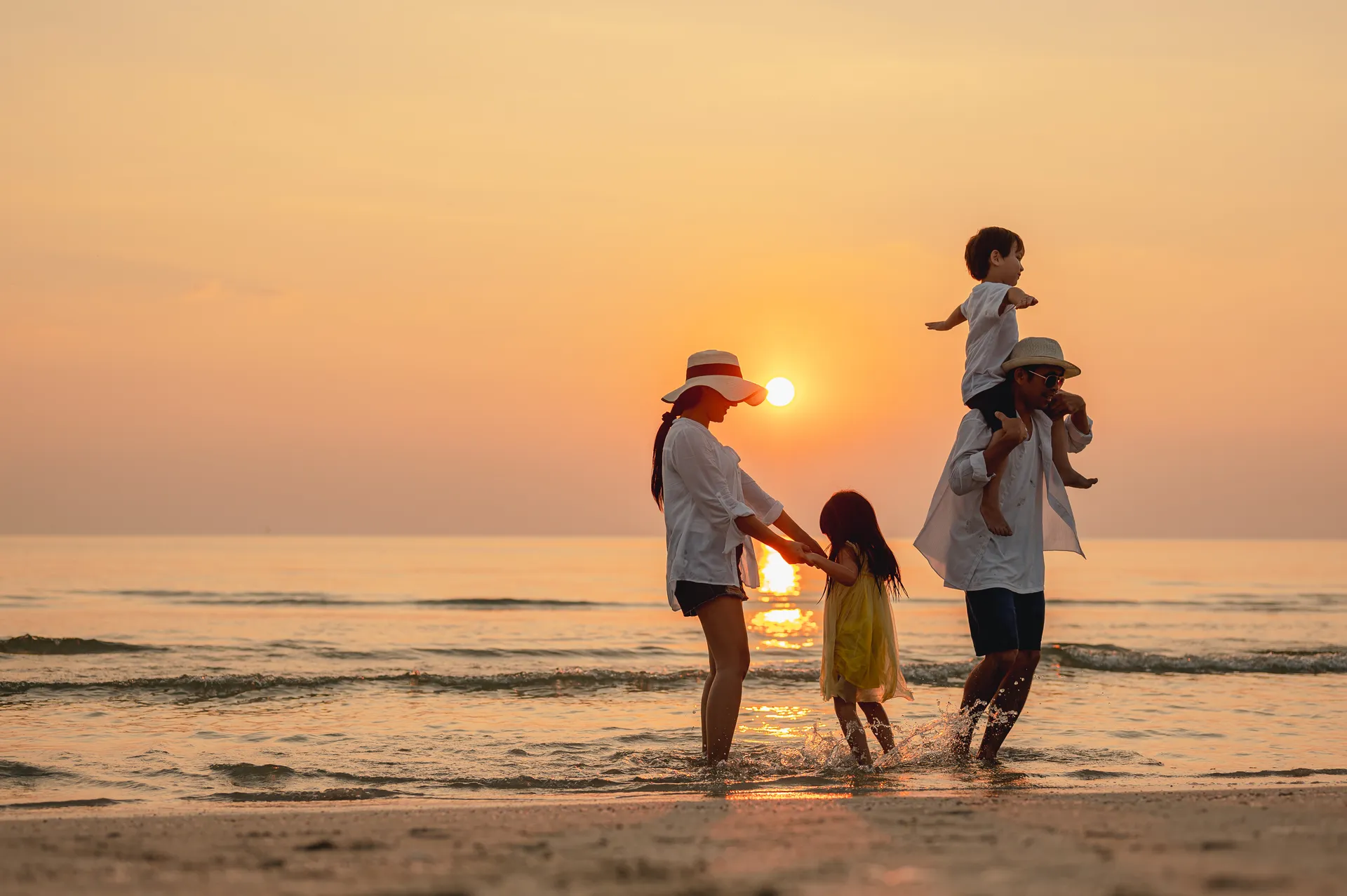 Familie mit zwei kleinen Kindern spielt bei Sonnenuntergang in der Brandung am Strand nahe Ocean House Zandvoort