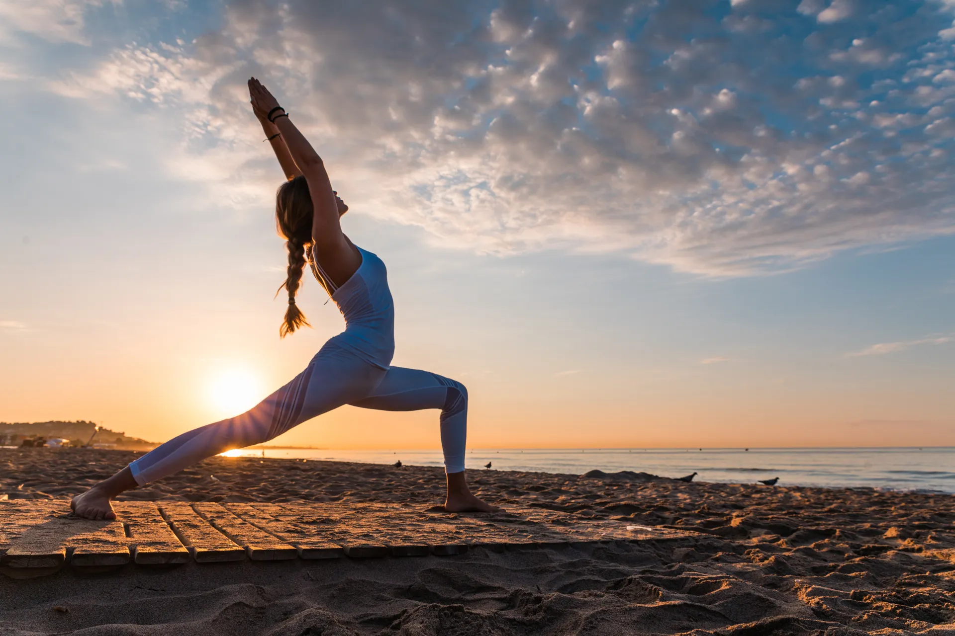 Frau in einer Yogapose am Strand bei Sonnenaufgang, Teil des Wellness Beach Retreat mit Zenzo Yoga und Ocean House Zandvoort